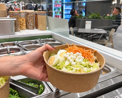 Una pokè con insalata, uovo sodo, mozzarelline e carote, tenuta in mano sopra il bancone di POK&DINA